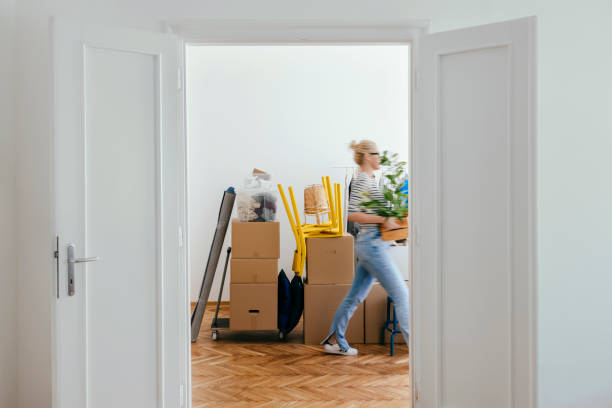 Unrecognizable woman carrying and unpacking boxes in new home on moving day.